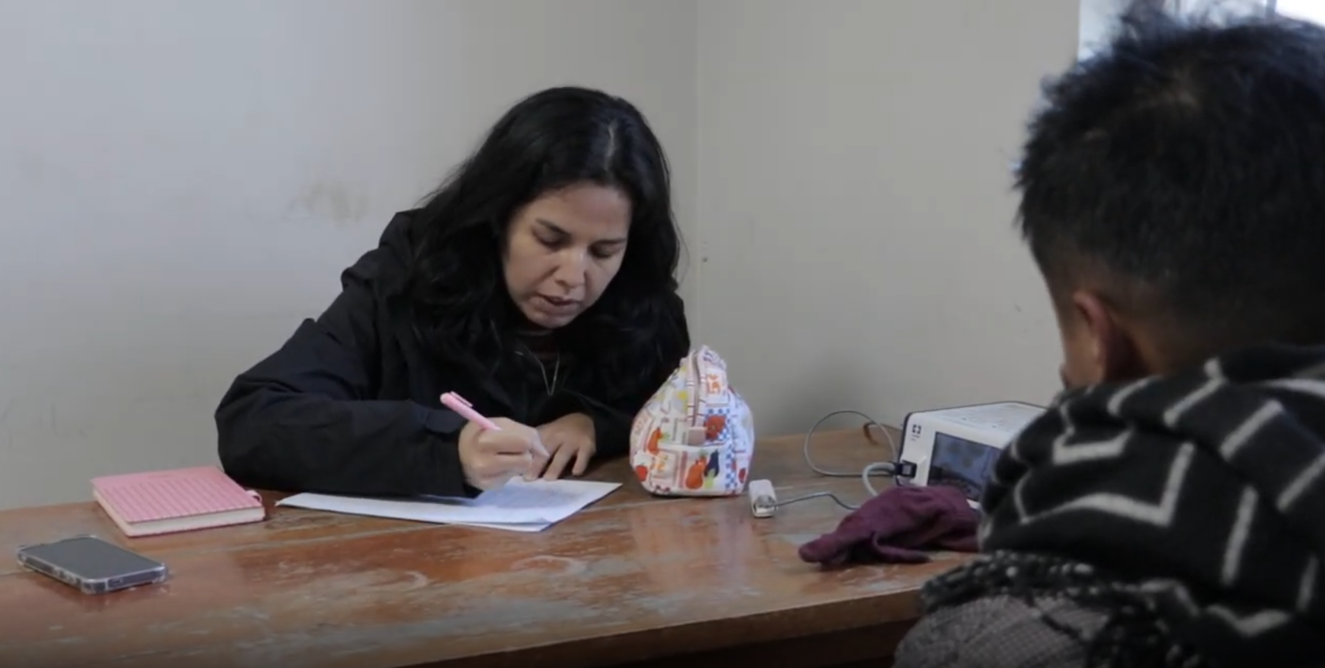 Researcher recording study information while a participant sits across the table during a field visit in Cerro de Pasco